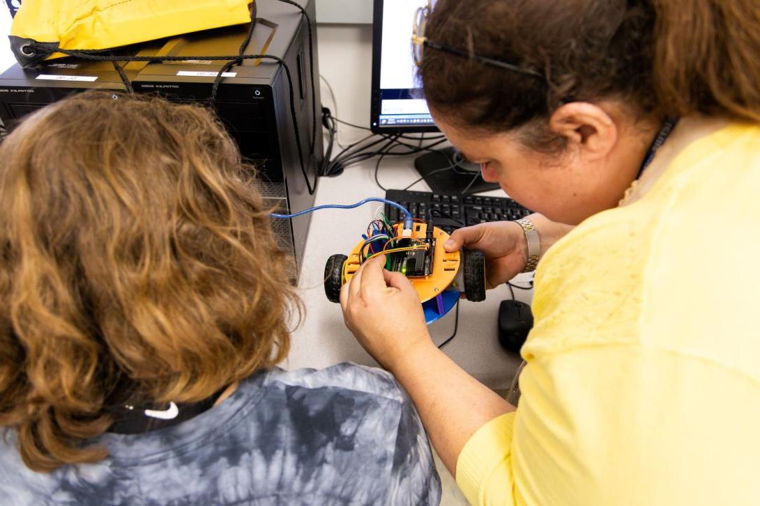 An instructor and young student in Kettering's Pre-College program study the wiring of a small yellow robot