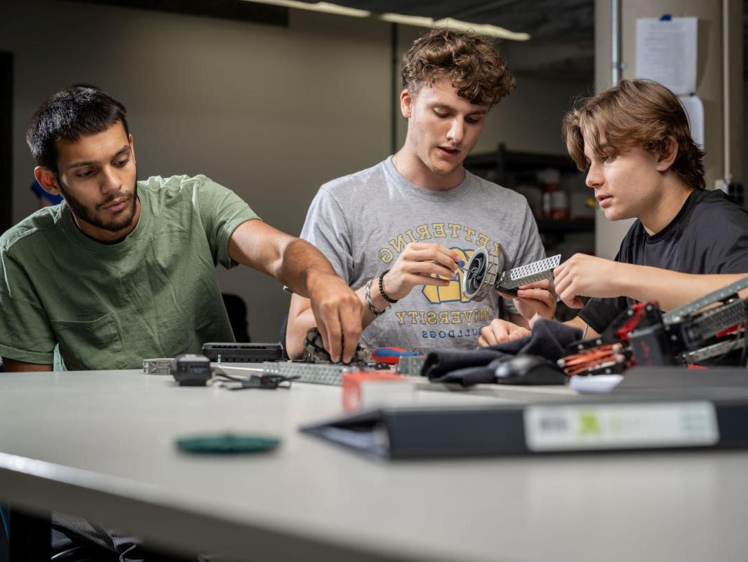 Three Kettering industrial engineering students inspect different machine parts and fit them together